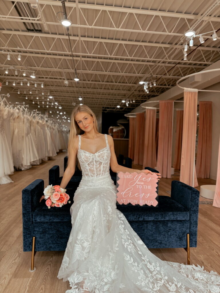 woman wearing a wedding dress comfortably setting on the couch holding a small flower bouquet and I said yes to the dress signage.