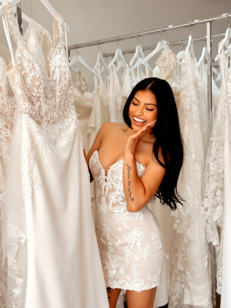 Bride smiling while trying on a lace wedding dress during a bridal appointment at Vow Ready.