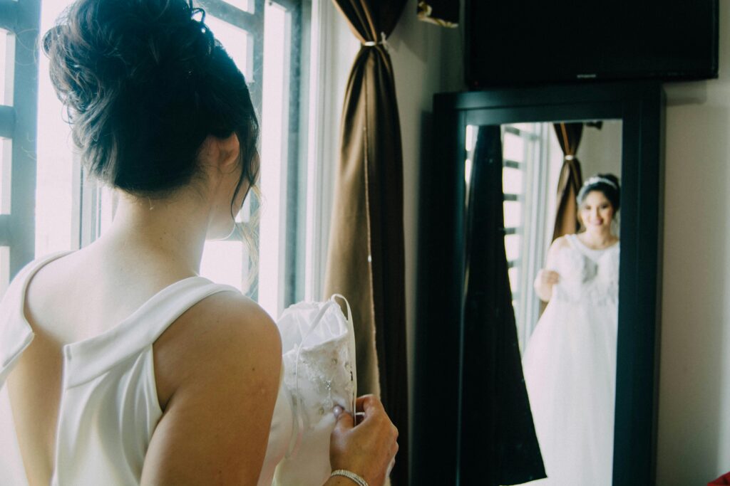 Happy bride fitting wedding dress looking at her reflection on the mirror.