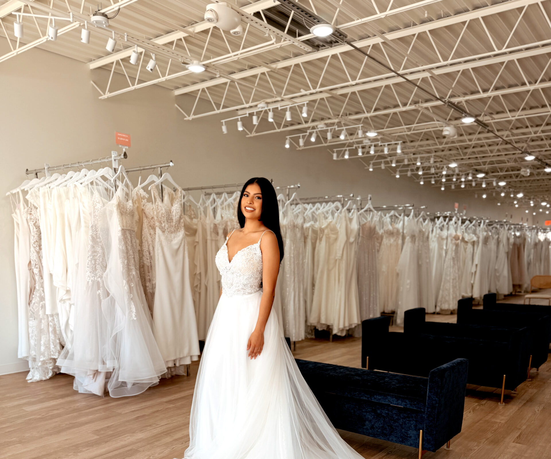 Bride modeling an off-the-rack lace wedding dress with a fitted silhouette and long lace train at a bridal store.