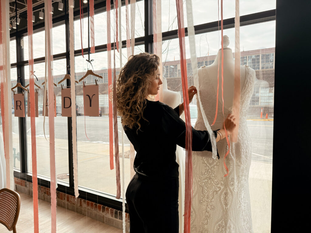 Bridal stylist arranging an off-the-rack lace wedding dress on a mannequin inside Vow ready bridal store.